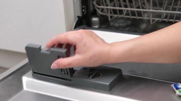 female hand puts dishwasher tablet into open automatic built-in dishwasher machine. Close up. video