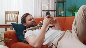 Portrait of young man lying on couch, using smartphone share messages on social media application video