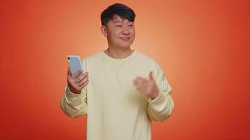 Happy asian man using smartphone pointing empty place, advertising area for mobile application video