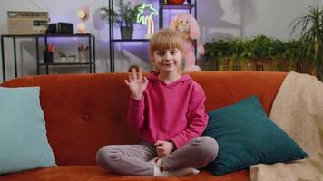 Child kid girl smiling friendly at camera, waving hands gesturing hello hi greeting at home on couch video
