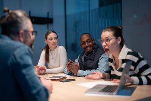 A diverse team of young professionals collaborates in a modern office conference room. Businesspeople discuss strategy, technology, and planning, using laptops to develop an innovative e-commerce photo