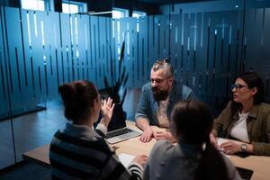 A diverse team of young professionals collaborates in a modern office conference room. Businesspeople discuss strategy, technology, and planning, using laptops to develop an innovative e-commerce photo