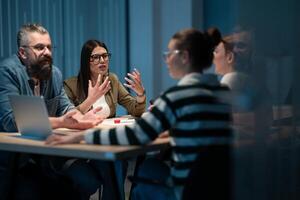 A diverse team of young professionals collaborates in a modern office conference room. Businesspeople discuss strategy, technology, and planning, using laptops to develop an innovative e-commerce photo