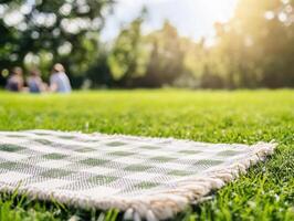 Picnic blanket on green grass in a park, bathed in sunlight. People enjoy the day in background photo