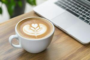 Latte art adorns a warm drink beside a modern computer, resting on a wooden desk's surface photo