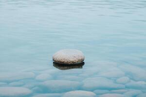 Zen stone resting on a calm, light blue water surface, creating ripples and a serene scene photo