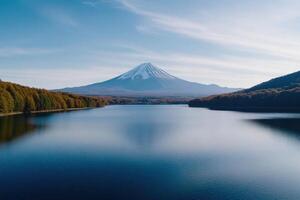 Snow-capped peak of mountain over serene lake, surrounded by autumnal trees in clear daylight photo