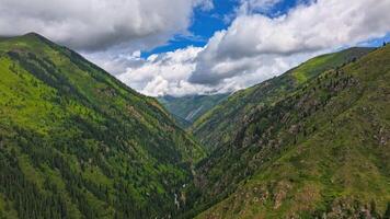 green mountains with white clouds on blue sky above, drone hyperlapse video