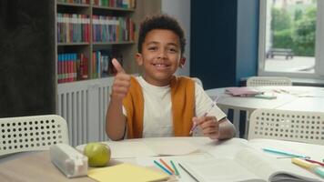 Little boy African American child pupil student smiling positive happy schoolboy son kid studying write exercise in classroom learn at table looking at camera thumb up like elementary school education video
