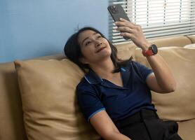 Woman lying down on sofa using mobile phone shopping online, watching social media network, relaxing lifestyles at home photo