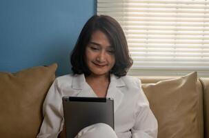 Business woman sitting on sofa holding tablet watching social media online ,using call with friend, checking email, after work lifestyles concepts photo