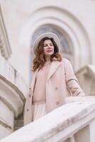 woman in elegant coat and hat against an intricate architectural backdrop, harmoniously blending modern fashion with historical allure. The soft daylight adds to its timeless appeal. photo