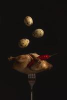 Quail fork eggs. Fried quail on a fork close-up on a black background serhu three quail eggs fly under the wing of a red hot pepper pod. vertical photo. photo