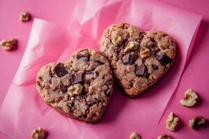 Heart-shaped chocolate chip cookies with walnuts on pink background photo
