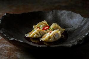 Delicious asian dumplings with soy sauce and red chili in black bowl photo