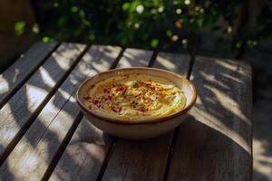 Creamy hummus garnished with paprika and olive oil on wooden table in sunny garden setting photo