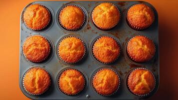 Perfectly baked muffins in a tray with a warm orange background enhancing their golden hue photo