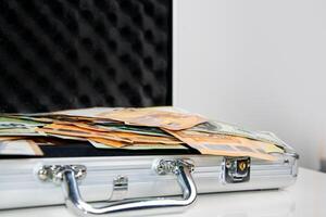 A close-up shot of a silver briefcase lying open on a white surface, revealing stacks of Euro bills inside photo