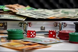 Close-up of red dice and stacks of poker chips on a white surface. A silver suitcase filled with money is visible in the background photo