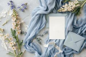 A beautifully arranged flat lay features wedding invitation cards atop a soft blue fabric, accompanied by vibrant flowers and decorative lace photo