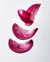 Four pieces of a red onion are suspended in the air, revealing their delicate layers and rich color. This unique display emphasizes their natural texture and appeal photo