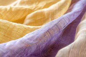 Textured fabric in shades of yellow and purple gently drapes, reflecting warm light and highlighting the delicate weave and color variations photo
