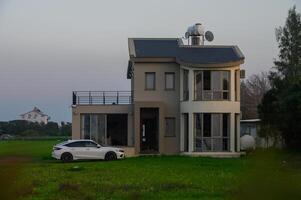 Modern house with a sleek car parked in front, surrounded by lush greenery during twilight hours photo
