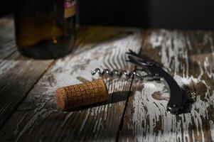 Corkscrew and cork resting on rustic wooden table with a bottle in the background at evening light photo