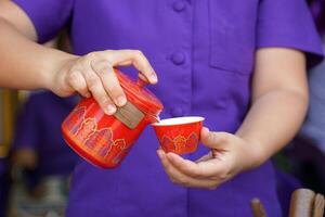 red Chinese pattern teapot is held in the hand and pouring tea into a teacup, which is a Chinese tea drinking culture. photo