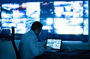CCTV operator is sitting and recording the time on a laptop monitor on a piece of paper. photo