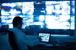 A cctv officer is sitting and checking images from a cctv camera displayed on a laptop screen. photo