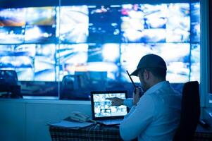 a man sitting at a desk with a laptop computer with multiple monitors photo