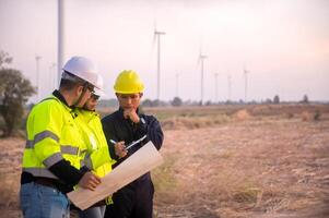 three men in hard hats and safety vests standing in front of wind turbines photo