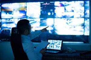 CCTV officer sitting and checking reports on clipboard. along with pointing at multiple monitors photo