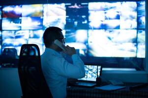 CCTV operator is talking on the phone to inform about the incident that is happening on multiple monitors. photo