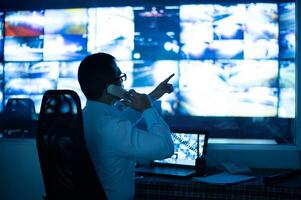 The CCTV operator is talking on the phone and pointing at the monitor to check the image on the screen. photo