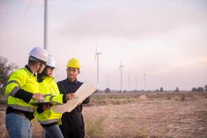 A team of maintenance engineers is planning the maintenance of wind turbines in a field photo