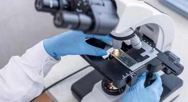A person in a white lab coat is using a microscope photo