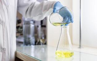 A person in a lab coat pouring yellow liquid into a beaker photo