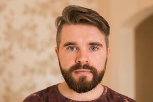 Portrait of an attractive young bearded hipster man looking at the camera standing in modern house, wearing a casual shirt. The view while the calling concept, call portrait photo