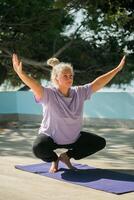 Mature woman with dreadlocks working out doing yoga exercises on sea beach - wellness well-being and active elderly age concept photo