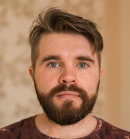 Portrait of an attractive young bearded hipster man looking at the camera standing in modern house, wearing a casual shirt. The view while the calling concept, call portrait photo