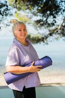 Old woman with dreadlocks walking with her mat to yoga or pilates class in park copy space - well being and leisure activity concept photo