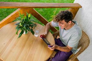 Young man playing game drinking water at terrace in summer day. Technology and game addiction concept photo