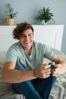 Handsome excited gamer sitting on a bed and playing games on a console. Wireless controller and online game technologies concept photo