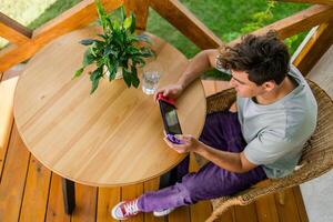 Young man playing game drinking water at terrace in summer day. Technology and game addiction concept photo
