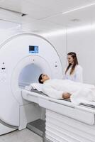 Female doctor is preparing patient for magnetic resonance procedure. Patient is lying at CT scanner bad and waiting to be scanned. Medical Lab with High-Tech Equipment. Vertical shot photo