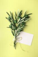 Olive branch with green olives and blank card on light yellow background. Nature-inspired mockup and eco-friendly concept. photo