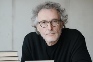 Close up mature man writer with glasses sitting at a desk surrounded by books. photo