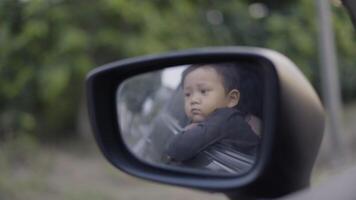 Happy child looking out of open car window while driving along a country road. video